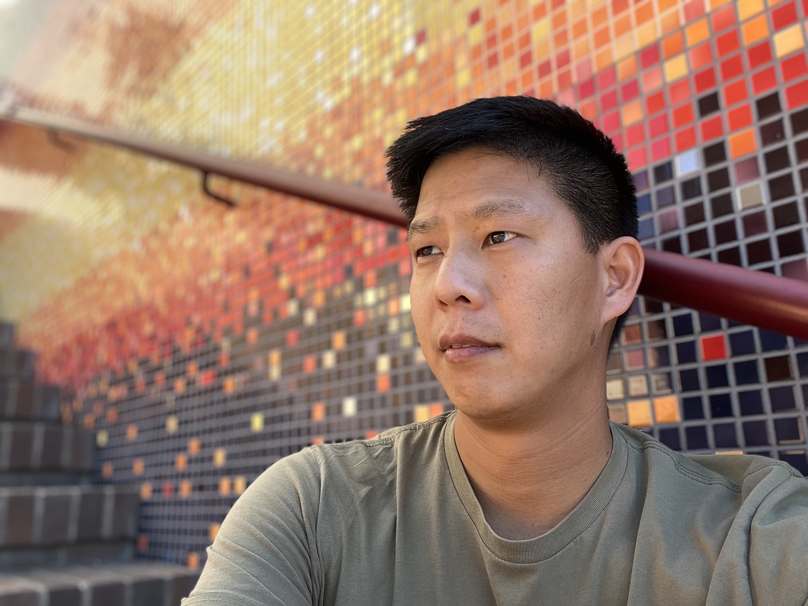 Asian male with short black hair sitting against mosaic tiles