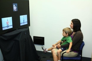 A toddler sitting on his mother's lap watching a video on a large television screen.