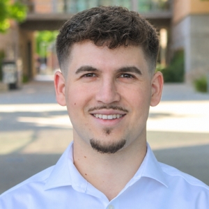 Man in white shirt smiles at camera on sunny day.